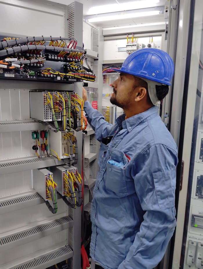 why-choose-us-03 Electrician in blue helmet checking control panel wiring for safety compliance.